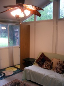 Front room showing futon, one closet, eaves' windows, overhead fan and windows toward front yard.